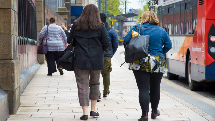 Two overweight women walk in city street while bus passes