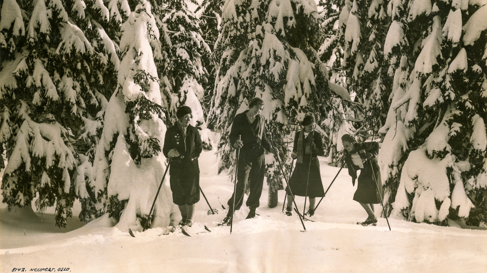 Girlfriends skiing under snow-covered trees, 1920