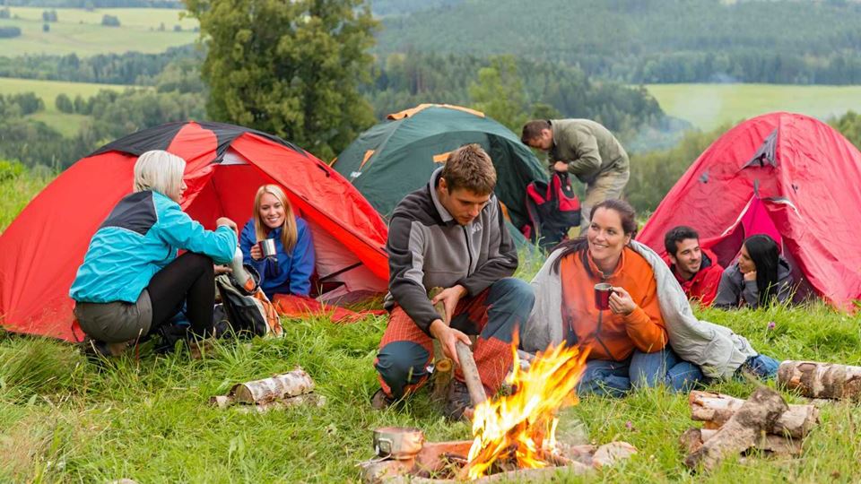 A group of friends at a campsite: pitched tents and a campfire in an open field
