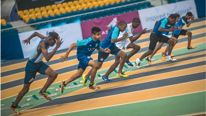 Young people sprint from the starting blocks on an indoor track