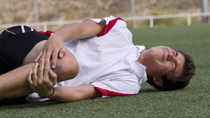 Fotballspiller med kneskade vrir seg på gressmatta