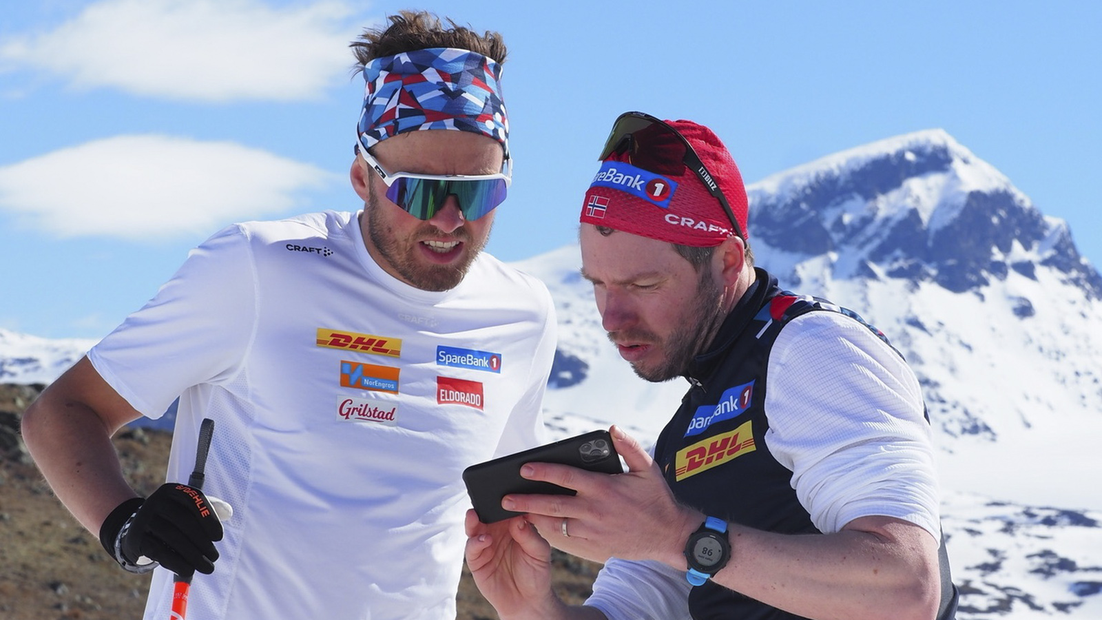 Emil Iversen og Eirik Myhr Nossum ser på mobil ute i solskinet på fjellet.