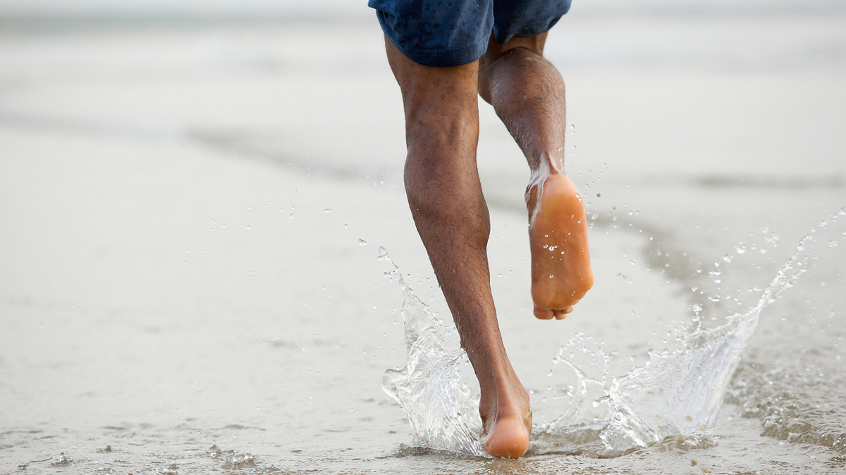 Legg-mukelsene av en mann som løper på strandet