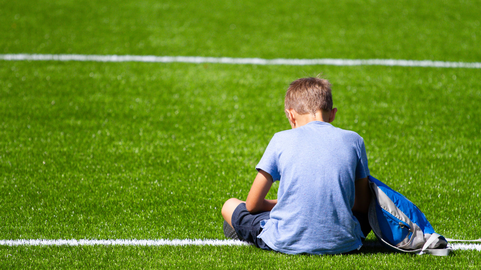 Guttunge sitter alene på en fotballbane