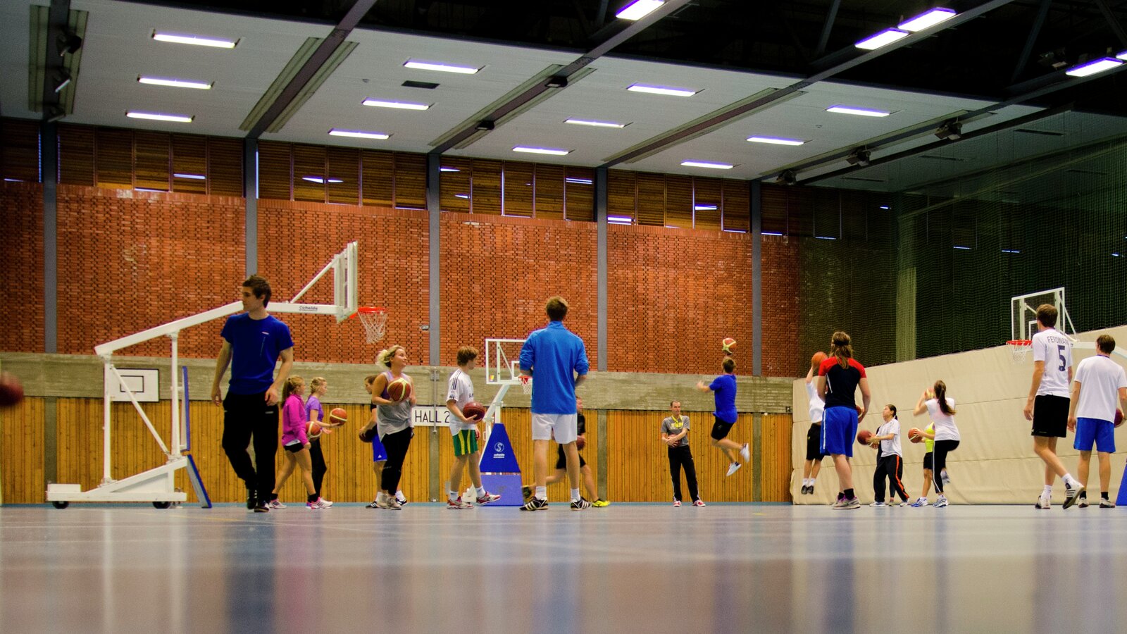 Studenter spiller basketball under kroppsøvingtimen i gymsalen. 