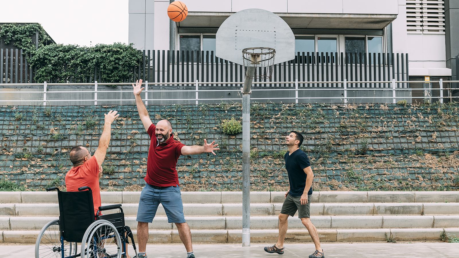 Tre venner spiller basketball, en er i rullestol