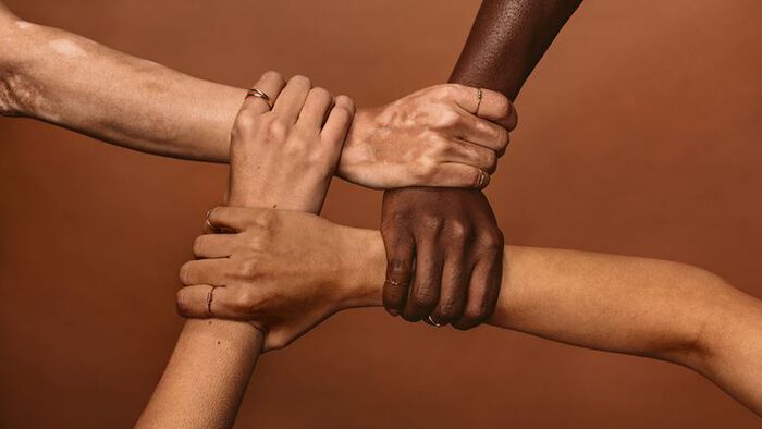 Fire mennesker med ulike hudfarger holder hender. 