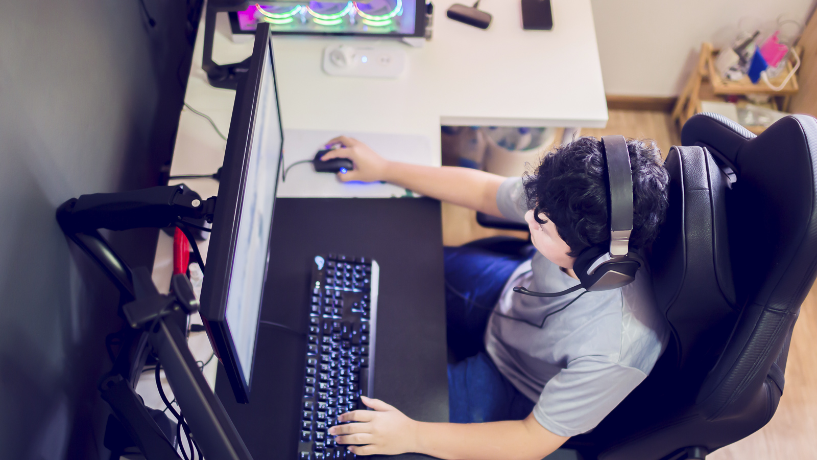 En gutt sitter foran PC med ørerklokker og gaming tastetur